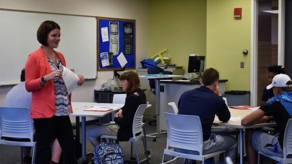 Associate professor walking in a classroom with college students at their desks